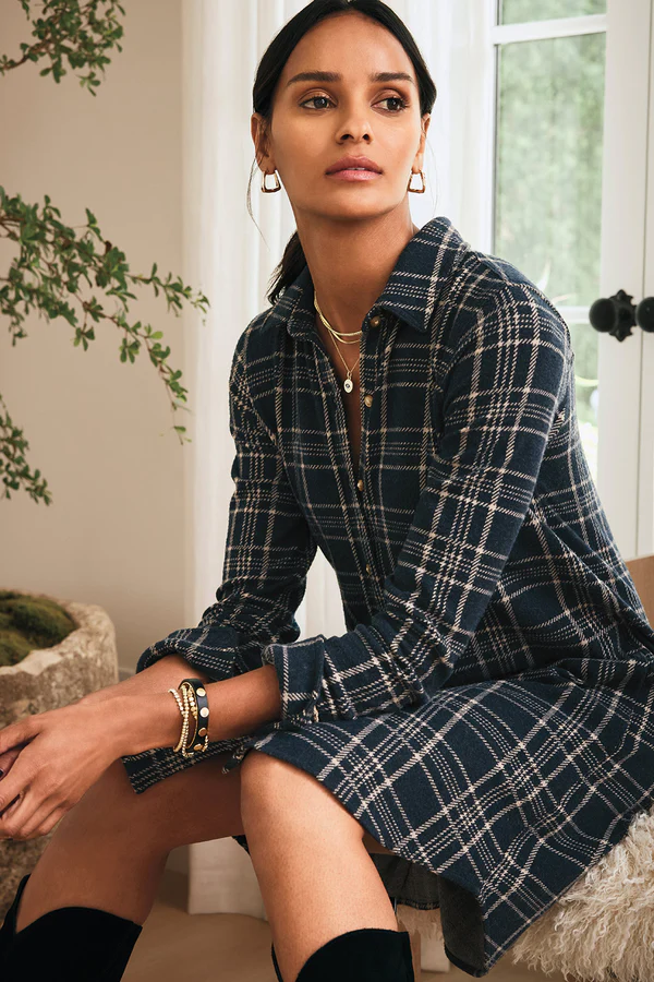 Chic plaid outfits for women showcasing a navy and white plaid shirtdress styled with layered gold necklaces, stacked bracelets, and black boots, perfect for a polished fall look