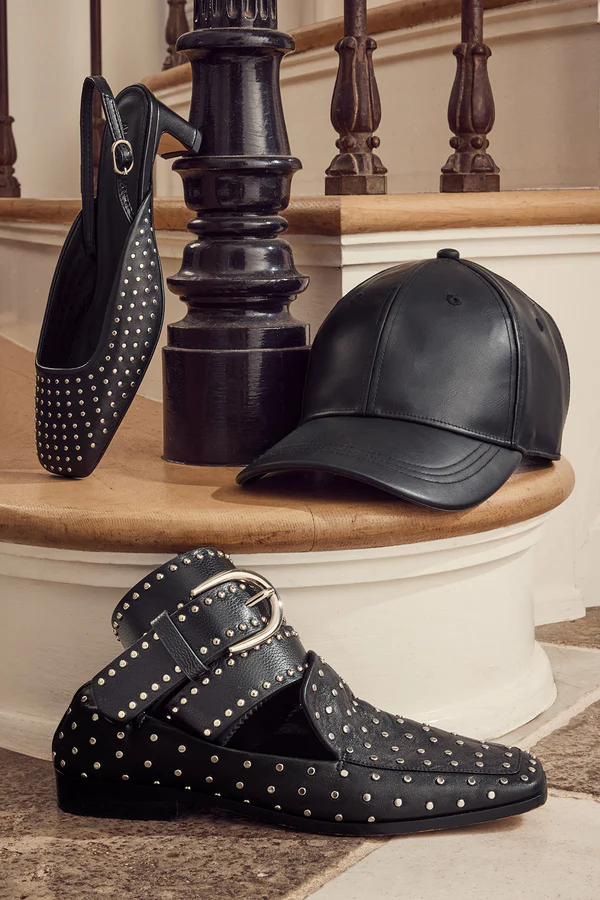 Stylish leather accessories including a studded loafer, leather baseball cap, and studded belt, showing how to layer with leather through accessories