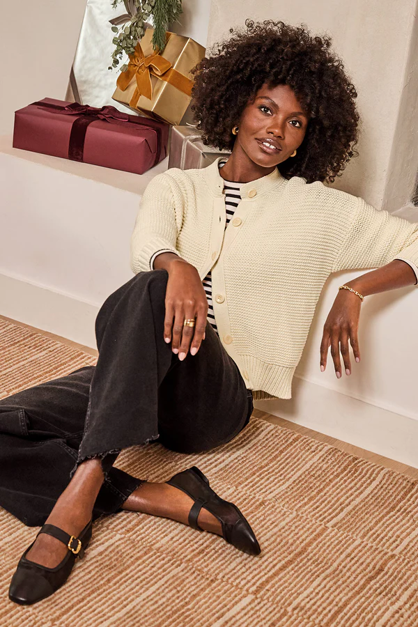 A cream cardigan layered over a striped top with black pants, illustrating what to wear for family photos with coordinating neutral tones