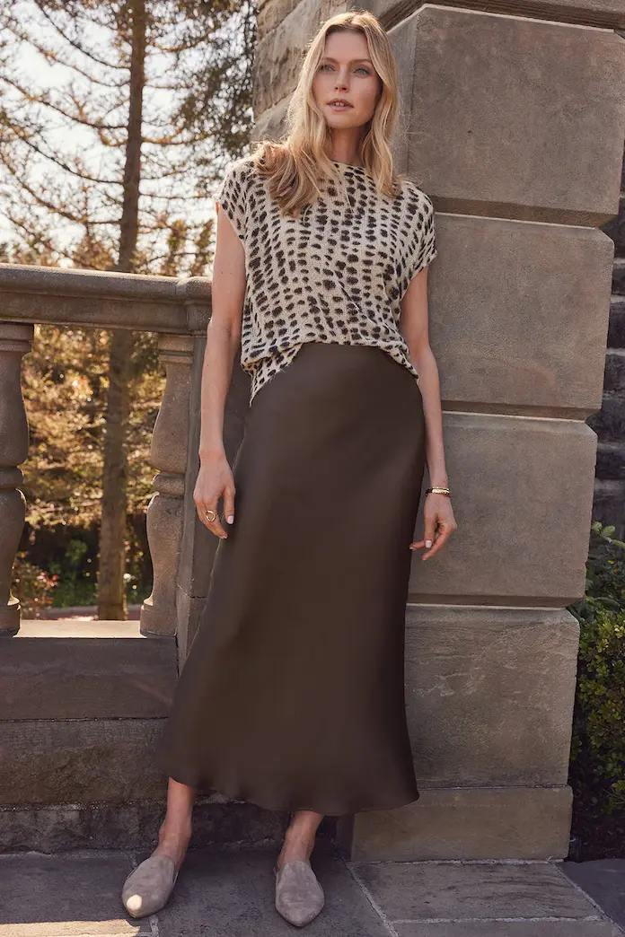 A woman styled in a patterned top and a satin maxi skirt, offering an elegant contrast to the classic denim midi skirt for a sophisticated fall look.